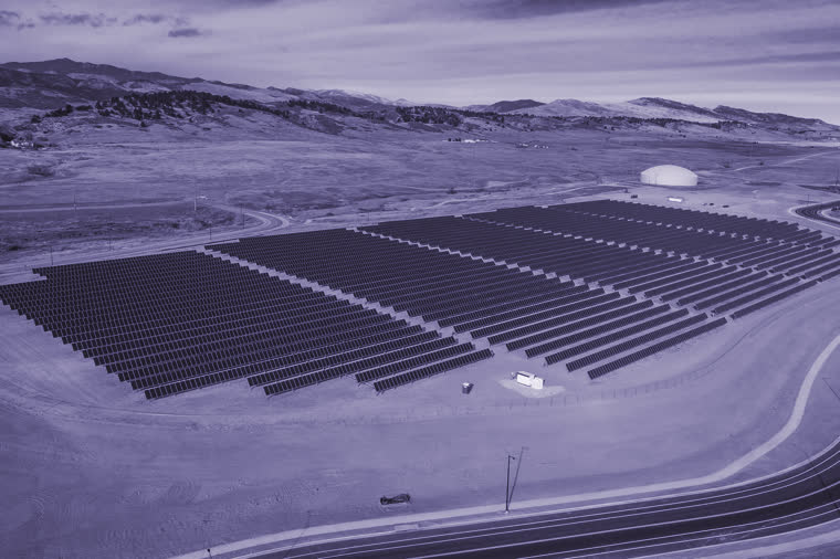 Rows of solar panels on a wide bench of dry open ground, hills behind.