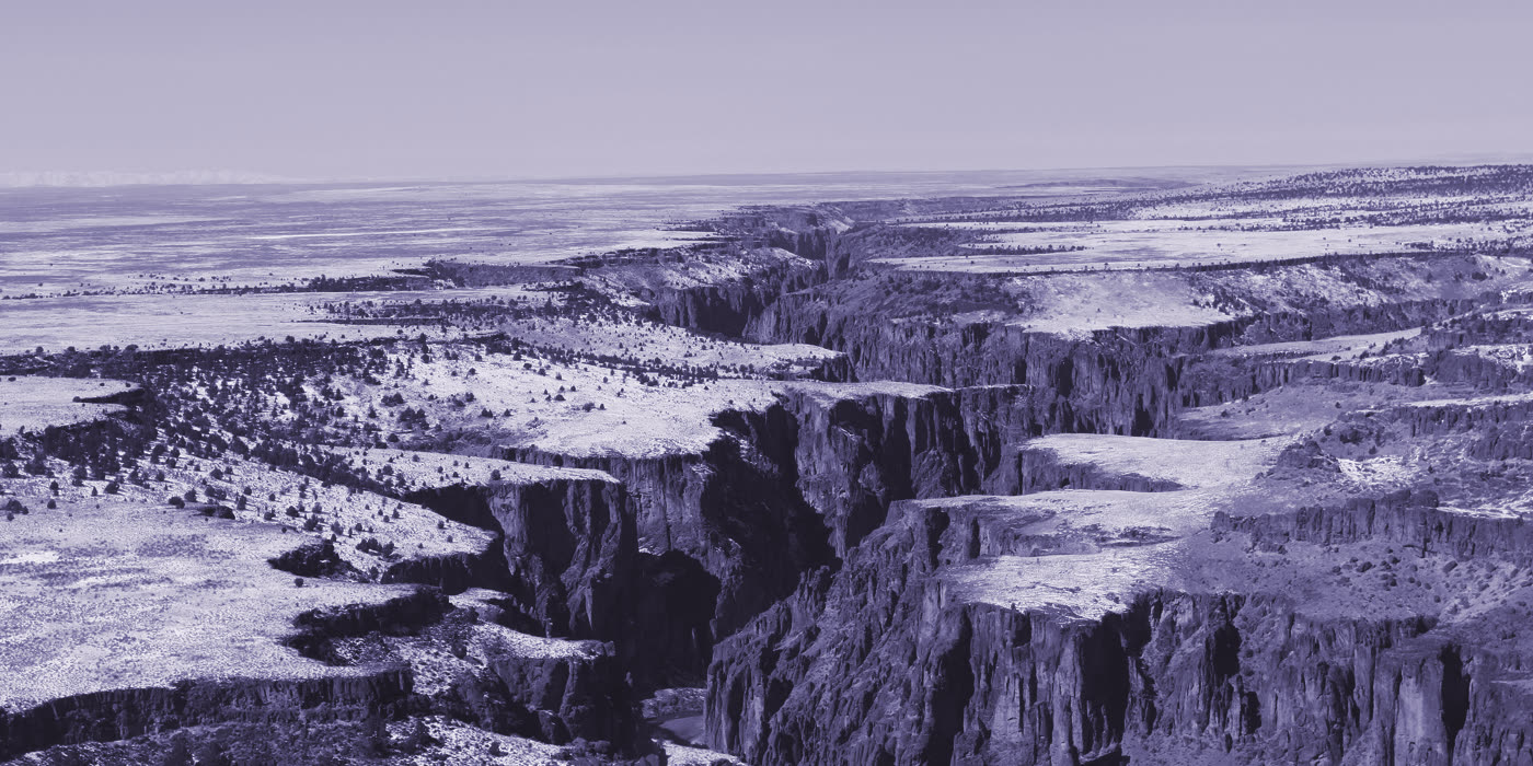 Canyon rimrock cutting through an open high desert bench, dusted with snow.